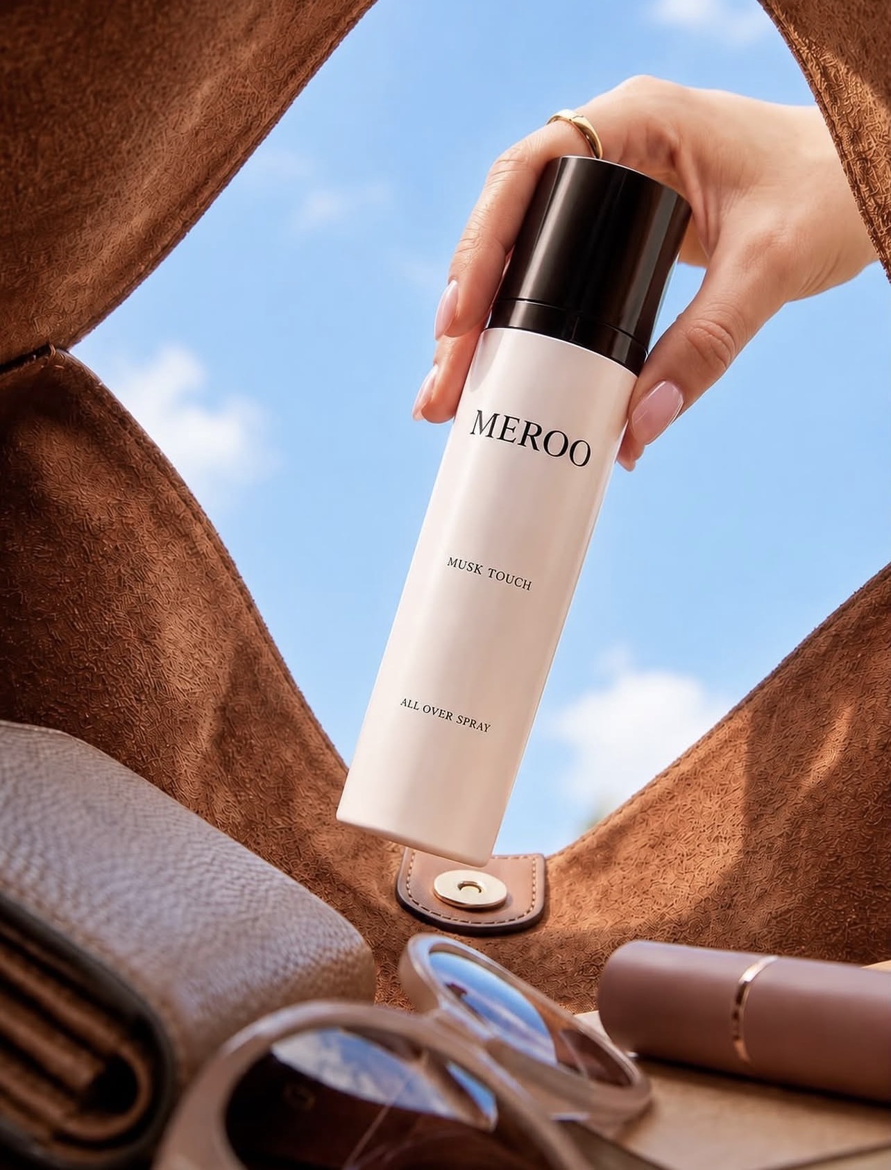 MEROO Musk Touch All Over Spray held against a blue sky — campaign image by By Amerra Mohammed